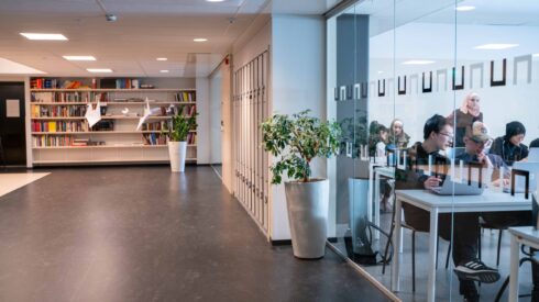 Korridor i skolan med glasvägg in till ett klassrum där elever jobbar på sina datorer