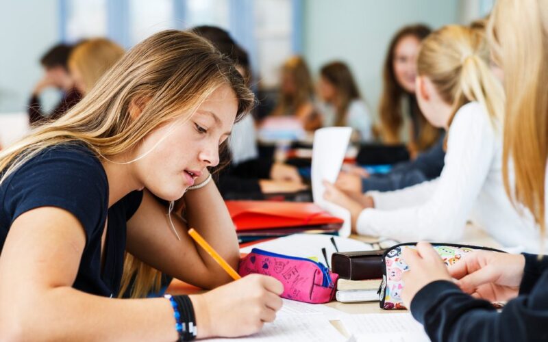 Kvinnlig elever sitter i klassrum och skriver i en bok